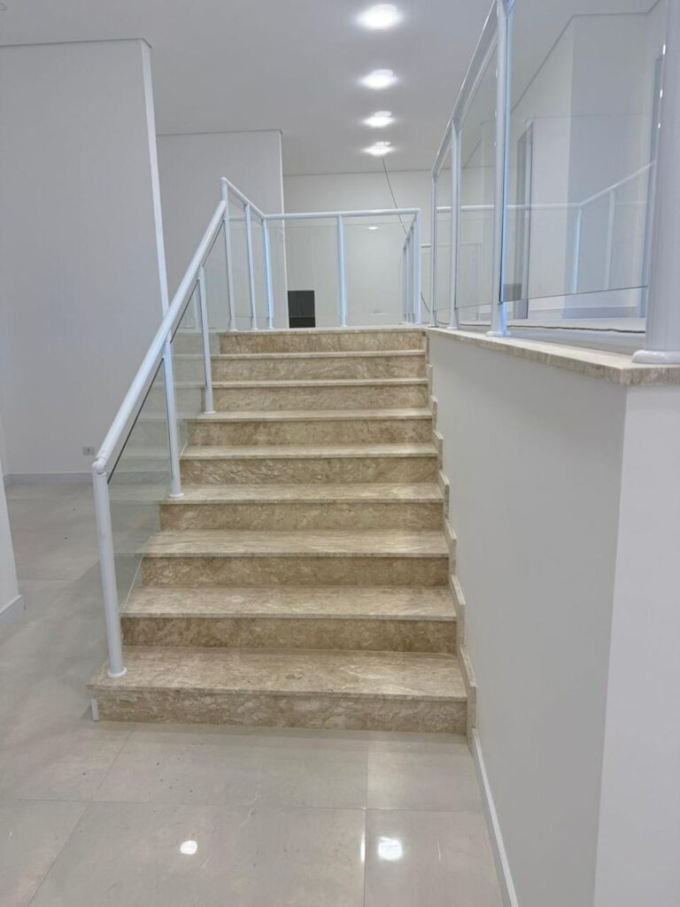 Escada em pedra bege com guarda-corpo de vidro